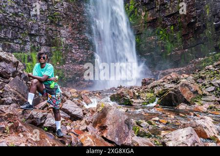 Woman stands among the rocks with a water bottle at Sweden's highest waterfall Njupeskär. Stock Photo