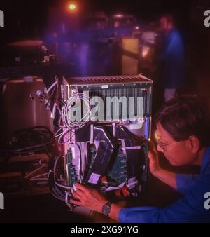Technician inspects modular electronic control unit with cables and circuit boards in dim lab, maintaining industrial computing system equipment Stock Photo