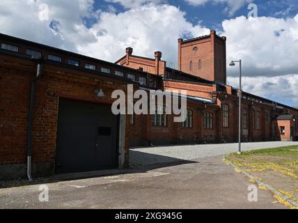 A historic brick industrial building with large arched windows and a prominent tower against a backdrop of a blue sky with scattered clouds. The build Stock Photo