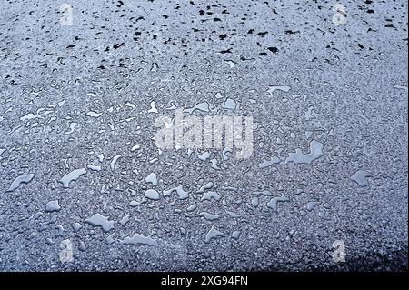 A close-up view of wet pavement covered in water droplets, creating a textured and reflective surface. The image captures the detail of the asphalt wi Stock Photo