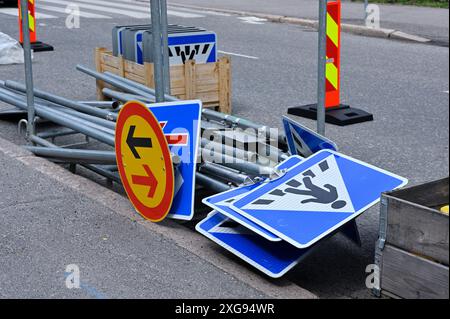 A collection of road signs and metal poles placed on the side of a street, likely for an ongoing or upcoming road construction project. The signs incl Stock Photo