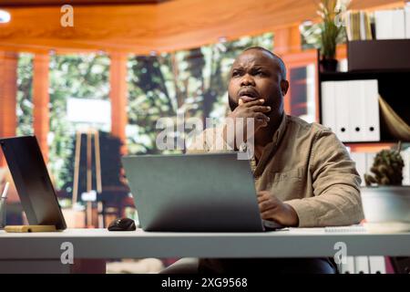 Freelancer managing startup projects and thinking about client needs from his home office, developing new growth strategy. Self employed analyst does telecommuting work on laptop. Stock Photo
