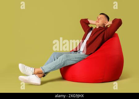 Handsome man resting on red bean bag chair against green background Stock Photo