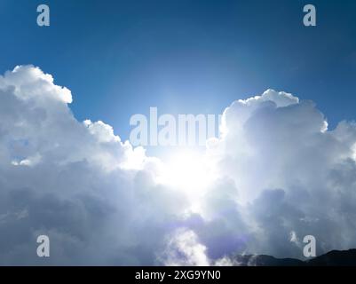 The sun shining through the puffy clouds above mountain Stock Photo