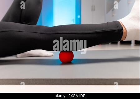 Close-up of self-massage of a sports woman indoors using a massage ball. Myofascial massage without a masseur. Elimination of pain in leg muscles Stock Photo