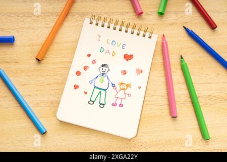 Fathers day concept. Notebook with drawing of a father with a girl and marker pens on a wooden table Stock Photo