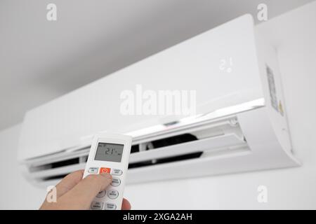Hand operating a Remote control of a Domestic Air conditioner unit mounted on wall Stock Photo