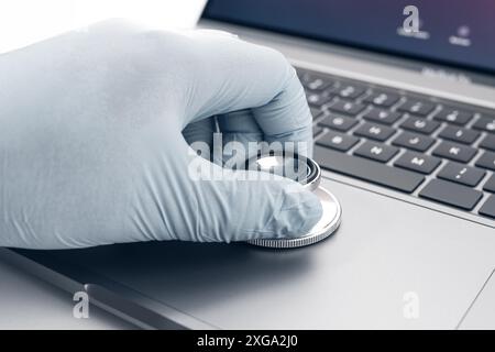 Hand holding a Stethoscope on modern laptop computer. Concept of a technician checking computer problems Stock Photo