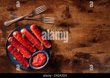 Sausages with ketchup and two forks, shot from the top on a dark rustic wooden background with copy space. Barbecue food Stock Photo