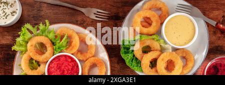 Calamari rings panorama. Squid rings with wine and various sauces, top flat lay shot on a dark rustic wooden table Stock Photo