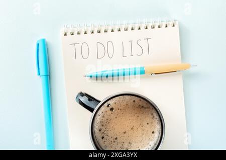 To do list. A paper notebook with a blue pen and a coffee mug, overhead flat lay shot on a blue background. The concept of planning Stock Photo