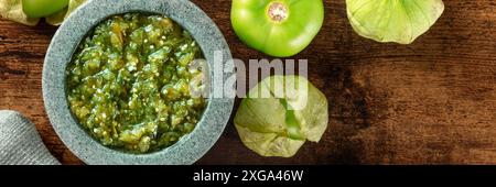 Tomatillos, green tomatoes, and salsa verde, green sauce, panorama with a molcajete, traditional Mexican mortar, overhead flat lay shot with copy Stock Photo