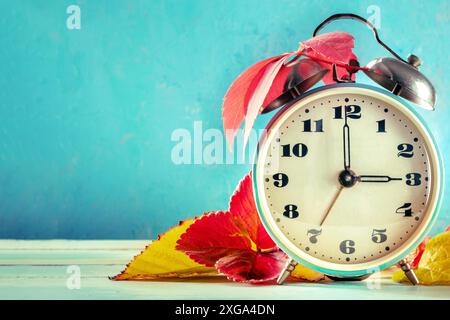 Daylight Saving Time concept, DST, fall back in autumn. A vintage alarm clock with autumn leaves on a blue background with a place for text Stock Photo