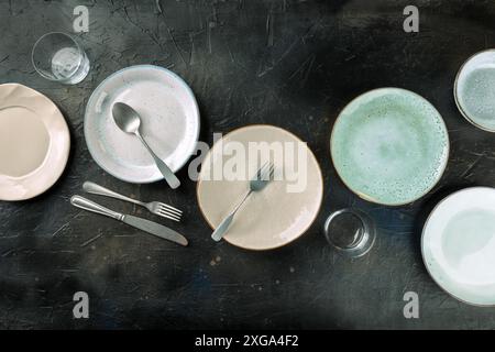 Modern tableware set with cutlery and glasses, overhead flat lay shot on a black slate background. Elegant dinnerware Stock Photo