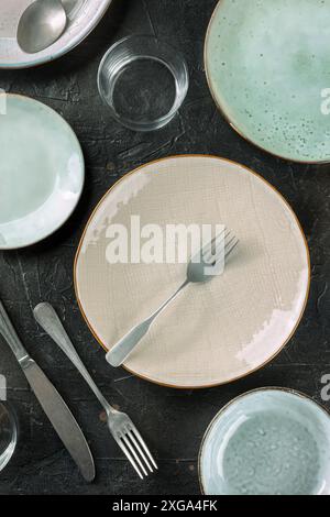 Modern tableware on a dark background. A plate with a fork, a glass and other dinnerware, top shot on a black table Stock Photo