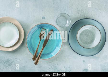Modern dinnerware with cutlery. A vibrant blue plate with a fork and a knife, top shot with a glass and other tableware Stock Photo