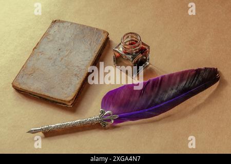 A quill pen, a vintage ink well, and an old notebook, retro objects on brown paper Stock Photo