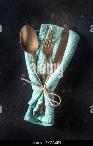 Cutlery. A spoon, a fork, and a knife in a blue napkin on a black background. Modern tableware on a dark table, shot from the top Stock Photo