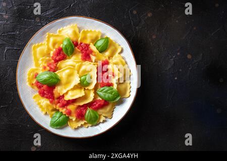 Ravioli with tomato sauce and fresh basil leaves, overhead shot with a place for text. Italian recipe on a black slate background Stock Photo