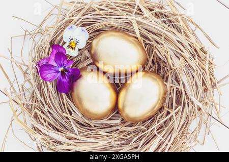 Easter golden eggs in a hay nest with flowers, overhead view on white background Stock Photo