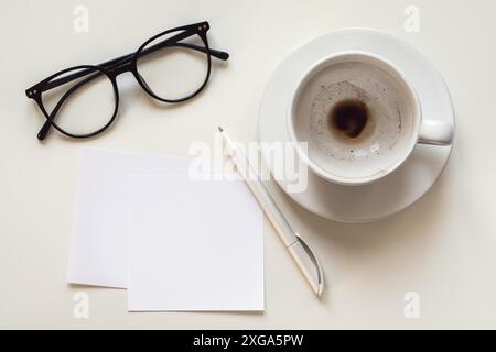 Paper notes mockup, blank space, empty coffee cup, eyeglasses and pen on white desk, overhead flat lay Stock Photo