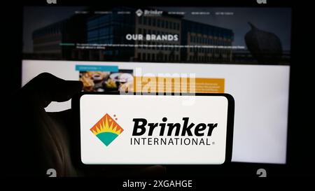 Person holding cellphone with logo of US hospitality company Brinker International Inc. in front of business webpage. Focus on phone display. Stock Photo