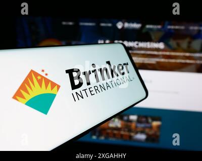 Mobile phone with logo of American hospitality company Brinker International Inc. in front of website. Focus on center-left of phone display. Stock Photo