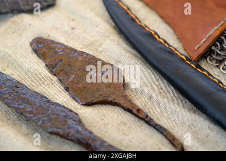 A pair of rusty metal knives are on a table next to a leather sheath. The knives are old and worn, and the sheath is brown and leathery. Concept of hi Stock Photo