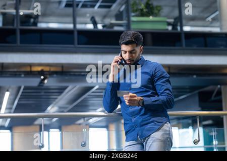 Talking on smartphone, man checking notes in modern office building, copy space Stock Photo