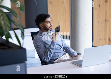 Using smartphone for voice command, man working with laptop in office Stock Photo