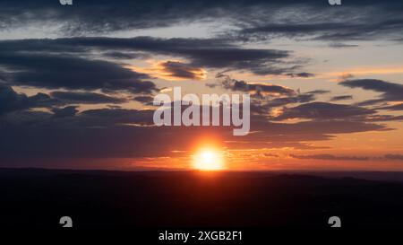Bright glowing sun setting behind countryside with bunch of clouds in sky Stock Photo