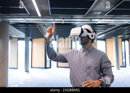 Using VR headset, man interacting with virtual interface in modern office, copy space Stock Photo