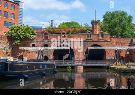 Black barge, lift bridge and trees at Castlefield Bridgewater Canal Basin, The Grocer's Warehouse, Manchester, UK, on a sunny June day with blue sky. Stock Photo