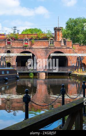 Black barge, lift bridge and trees at Castlefield Bridgewater Canal Basin, The Grocer's Warehouse, Manchester, UK, on a sunny June day with blue sky. Stock Photo