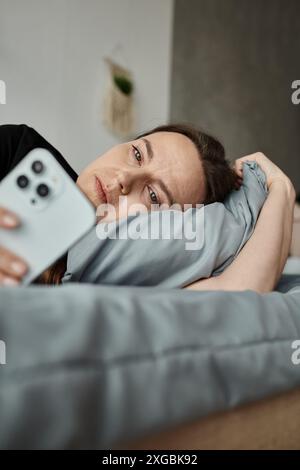 A woman resting in bed, engrossed in her phone screen. Stock Photo