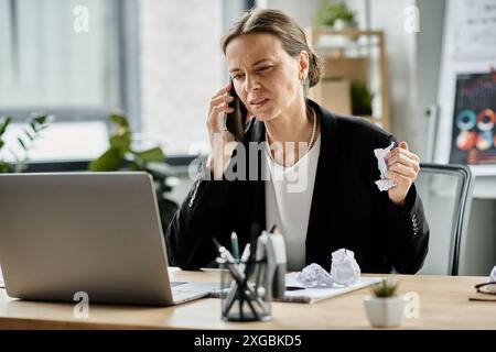 A middle-aged woman talks on the phone at her desk, showing signs of stress and mental fatigue. Stock Photo