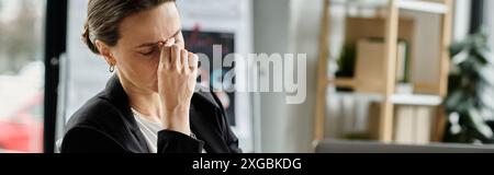Middle-aged woman sits at desk, covering eyes, stressed. Stock Photo