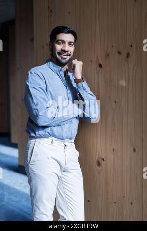 Smiling businessman in casual attire standing against wooden wall in office Stock Photo