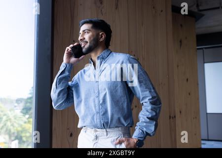 Talking on smartphone, man standing by window in modern office setting Stock Photo