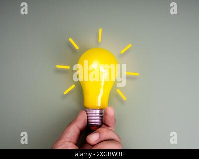 Glowing yellow lightbulb with radius graphic, neon style, holding by hand isolated on eco green background, minimal style. Closeup creative light bulb Stock Photo