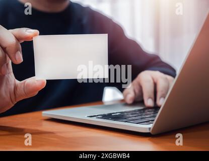 Business connection concept. Blank white plain name card showing by businessman hand, who working with laptop computer at workplace. Mockup business n Stock Photo