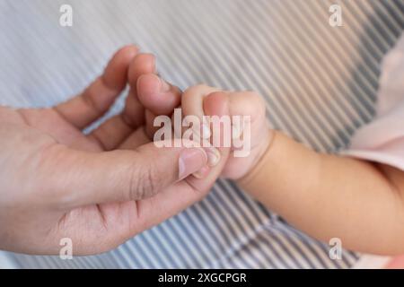 Asian parent hands holding newborn baby fingers, Closeup mother’s hand holding their new born baby day. Together love harmony peace family nursery hea Stock Photo