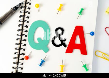 Blank multi-colored note paper with QA or questions and answers written on it. Top view of pen and glasses writing Q and A on desk. Selective focus. Stock Photo