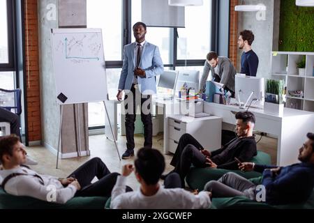 African American businessman presenting to his multiethnic colleagues his progressive ideas at a meeting in the spacious fashionably designed office r Stock Photo