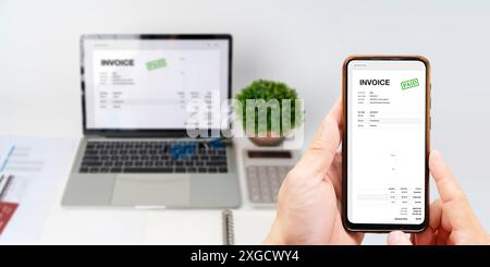 Digital Tax E Invoice Online Software On Laptop Screen. Close-up Of Businessperson Using Laptop While Paying Invoice On Mobilephone In Office. Stock Photo