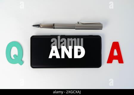 Q and A word on a smartphone and pen, white work desk background. Questions and answer concept. Selective focus,  flat lay. Stock Photo