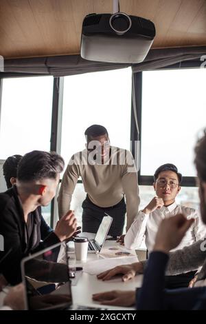 mixed race business team listening to african american male speaker discussing presentation on flip chart at meeting in boardroom, corporate training Stock Photo