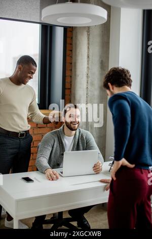 Group of three young multiethnic entrepreneurs standing in the office while debating and discussing new start-up project Stock Photo