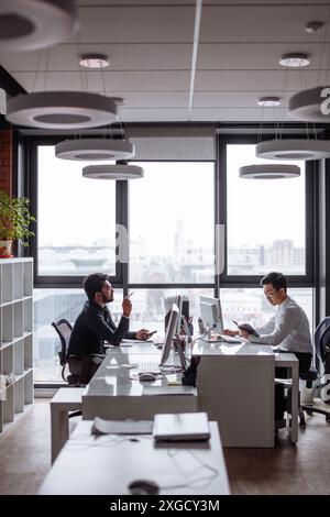Mix raced business partners planning next sales period. Indian and Chinese men in formal shirts discussing together business plan sitting opposite eac Stock Photo