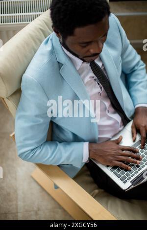 Successful African bearded entrepreneur in sky blue coat and tie serfing web sites with attentive and concentrated look, searching useful information Stock Photo
